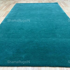 Puede incluir: Una alfombra rectangular de color turquesa con una textura suave y afelpada. La alfombra se muestra sobre un suelo de madera clara. El texto "ShamaRugsIN" est&aacute; impreso en la alfombra.