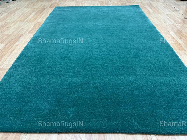Puede incluir: Una alfombra rectangular de color turquesa con una textura suave y afelpada. La alfombra se muestra sobre un suelo de madera clara. El texto "ShamaRugsIN" est&aacute; impreso en la alfombra.