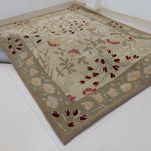 May include: A rectangular area rug with a floral pattern. The rug features a light green background with a repeating pattern of flowers in red, yellow, and cream. The border is a darker green with floral accents.