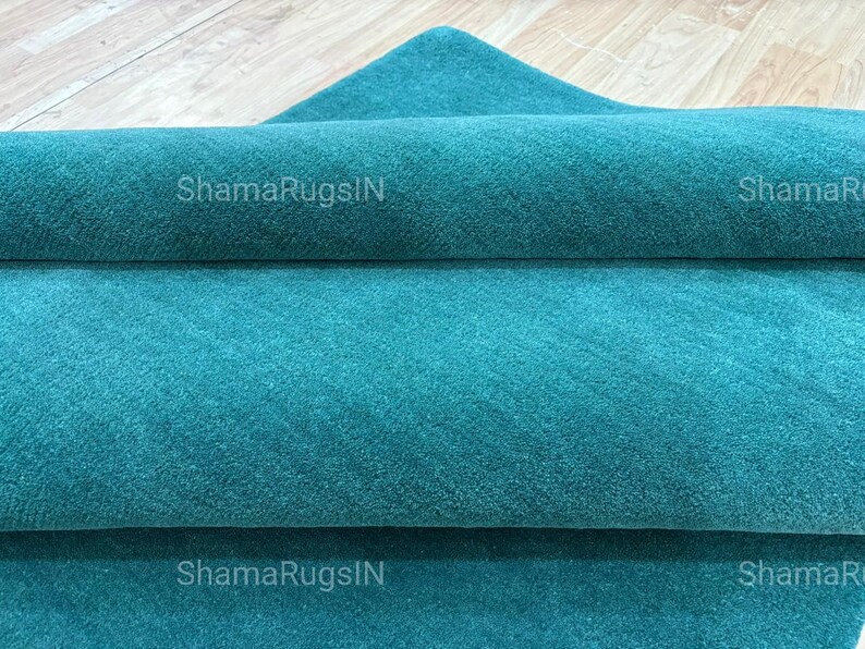 Puede incluir: Una alfombra turquesa enrollada con una superficie texturizada. La alfombra est&aacute; doblada sobre s&iacute; misma, revelando m&uacute;ltiples capas de la tela. El texto "ShamaRugsIN" es visible en la alfombra.
