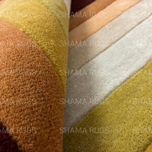 May include: Close-up of a multi-colored rug with a textured surface. The rug features a gradient of colors, including shades of yellow, orange, and brown. The text "SHAMA RUGS" is visible on the rug.