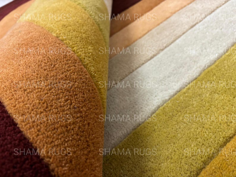 May include: Close-up of a multi-colored rug with a textured surface. The rug features a gradient of colors, including shades of yellow, orange, and brown. The text "SHAMA RUGS" is visible on the rug.