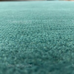 Puede incluir: Primer plano de una alfombra de color turquesa con una superficie texturizada. Las fibras de la alfombra crean una apariencia suave y afelpada. El texto "ShamaRugsIN" es visible.