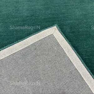 Puede incluir: Primer plano de una alfombra de color verde azulado con un reverso gris claro. La alfombra tiene una textura suave y afelpada y un borde gris claro. El texto "ShamaRugsIN" es visible en la alfombra.