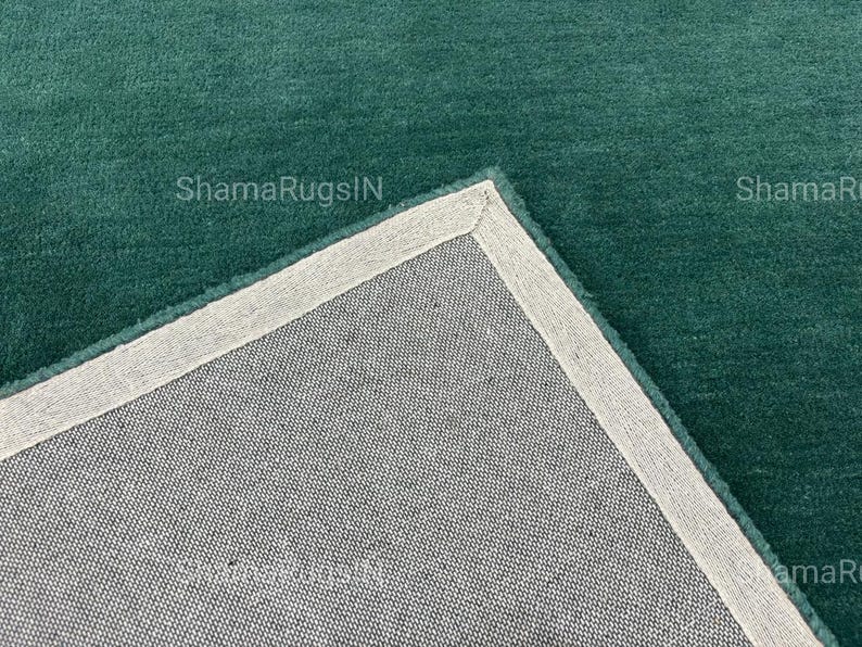 Puede incluir: Primer plano de una alfombra de color verde azulado con un reverso gris claro. La alfombra tiene una textura suave y afelpada y un borde gris claro. El texto "ShamaRugsIN" es visible en la alfombra.