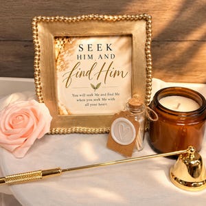 May include: A gold beaded frame containing text that reads SEEK HIM AND find Him, You will seek Me and find Me when you seek Me with all your heart. Includes a peach artificial rose, a small glass bottle with matches, a candle, and a gold wick dipper.