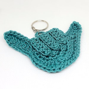 May include: Teal blue crocheted hand sign keychain with a silver metal ring.