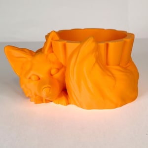 May include: Orange ceramic planter shaped like a fox curled up with its tail forming a pot.