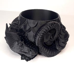 May include: A black dragon planter with a textured, scaly design. The dragon's head is curled around the planter's opening, creating a unique and decorative piece.