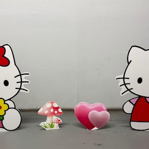 May include: White cartoon cat figures with black outlines, featuring a red bow, red flower, and holding flowers. A pink mushroom and two pink hearts are also present. These are likely decorative items.