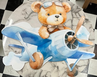 May include: A brown teddy bear wearing aviator sunglasses and a bow tie is flying a blue and white airplane with a propeller. The airplane is on a marble background.