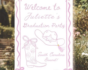 Può includere: Un cartello bianco su un cavalletto di legno con testo e illustrazioni rosa. Il cartello recita "Benvenuti alla festa di laurea di Juliette" con un cappello da cowboy e un'illustrazione di stivale. È incluso anche il testo "South Carolina Bound!"