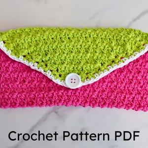 Könnte beinhalten: Eine gehäkelte Clutch mit einem Design in Limettengrün und Pink. Die Clutch hat einen weißen gehäkelten Rand und einen weißen Knopf.