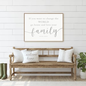 May include: A wooden bench with two pillows that say "welcome home" in a white farmhouse style entryway with a framed quote that reads "If you want to change the WORLD go home and love your family" and a potted plant.