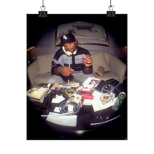 Könnte beinhalten: Poster-Druck mit einem Mann in einem schwarz-weiß gestreiften Hemd und einer Baseballkappe, der telefoniert. Auf einem Tisch vor ihm befinden sich ein Glas, ein Aschenbecher und eine Bierdose. Die Szene spielt in einem Innenraum.