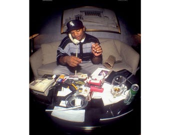 May include: A poster print showing a man in a black and white striped top and baseball cap, using a telephone. A table in front of him holds a glass, ashtray, and a can of beer. The setting appears to be indoors.