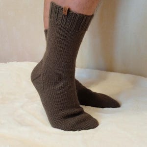 May include: A pair of brown knitted socks with a small brown leather tag on the top of one sock.