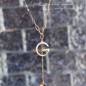 Puede incluir: Collar dorado con un colgante en forma de la letra "G". La cadena es fina y tiene un peque&ntilde;o dije circular. El texto "I look the moon, but only see you" es visible en el fondo.