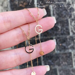 Puede incluir: Dos collares dorados con colgantes con la letra "G". Uno de los colgantes est&aacute; delineado en negro. Cada collar tiene una cadena delicada y un peque&ntilde;o dije redondo. La imagen incluye el texto: "I look the moon, but only see you."