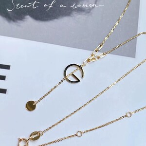 Puede incluir: Un delicado collar de oro con un colgante circular y un peque&ntilde;o dije de disco. El collar presenta una fina cadena y un cierre de broche. El texto "Scent of a women" est&aacute; en el fondo.