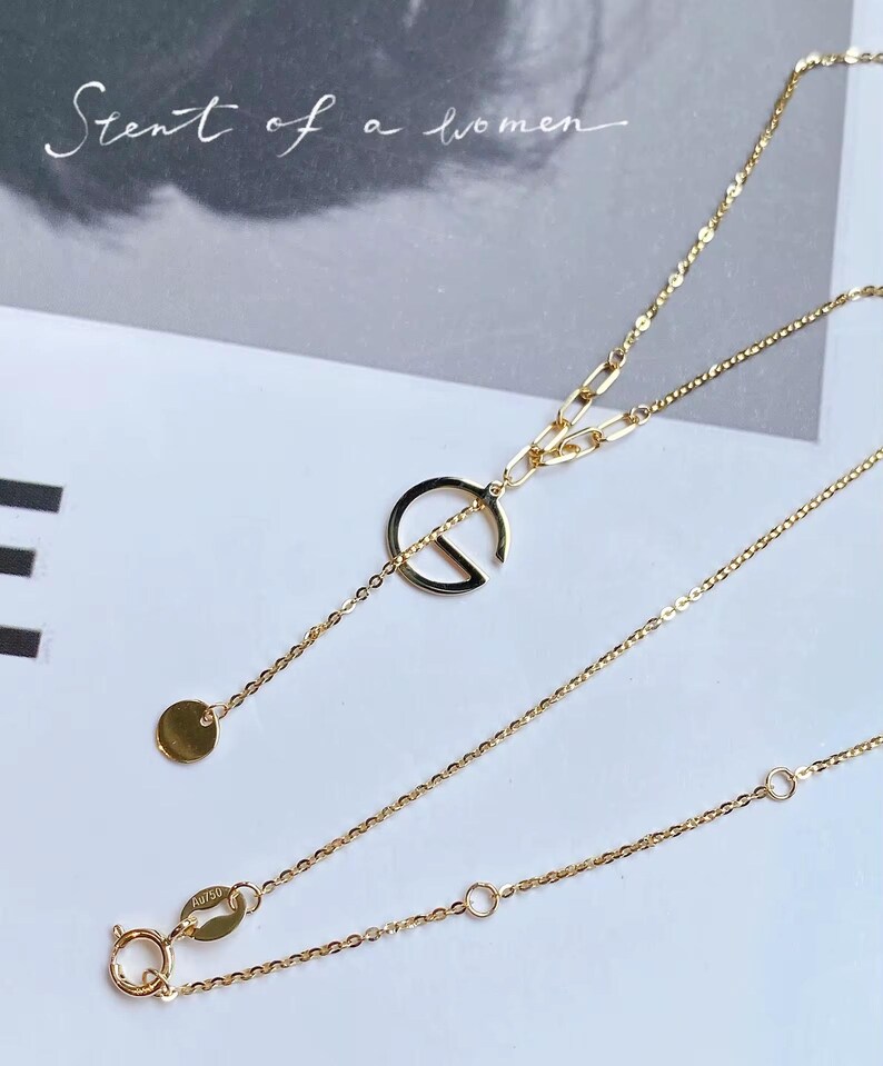 Puede incluir: Un delicado collar de oro con un colgante circular y un peque&ntilde;o dije de disco. El collar presenta una fina cadena y un cierre de broche. El texto "Scent of a women" est&aacute; en el fondo.