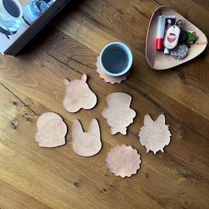 May include: A collection of light brown leather coasters in various cartoon character shapes, including a hippo, rabbit, and owl. A cup of tea sits on a matching coaster. A small leather tray holds keys and lip balm.