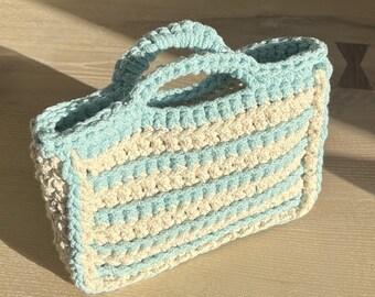 May include: A crocheted tote bag with a light blue and cream striped design. The bag has two handles and is made with a thick yarn.