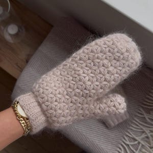 Peut inclure: Une paire de mitaines beige clair avec un motif floral textur&eacute;. Les mitaines sont faites d'une mati&egrave;re douce et duveteuse. Les mitaines reposent sur une couverture grise claire.