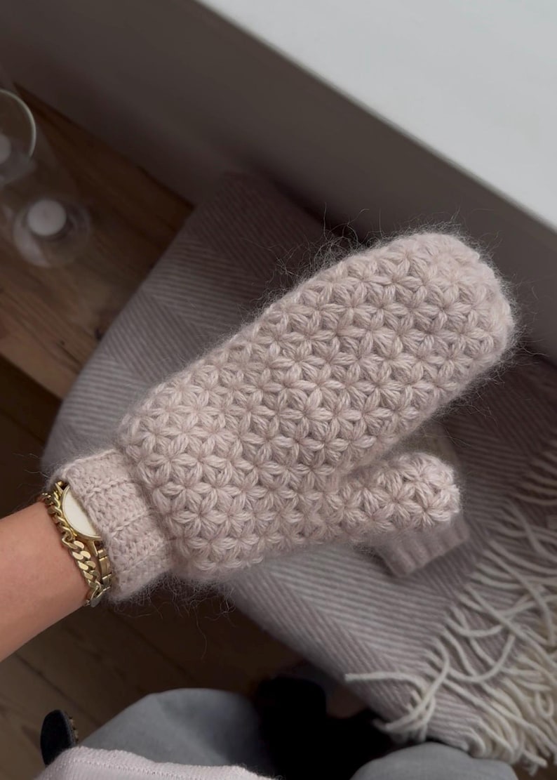Peut inclure: Une paire de mitaines beige clair avec un motif floral textur&eacute;. Les mitaines sont faites d'une mati&egrave;re douce et duveteuse. Les mitaines reposent sur une couverture grise claire.