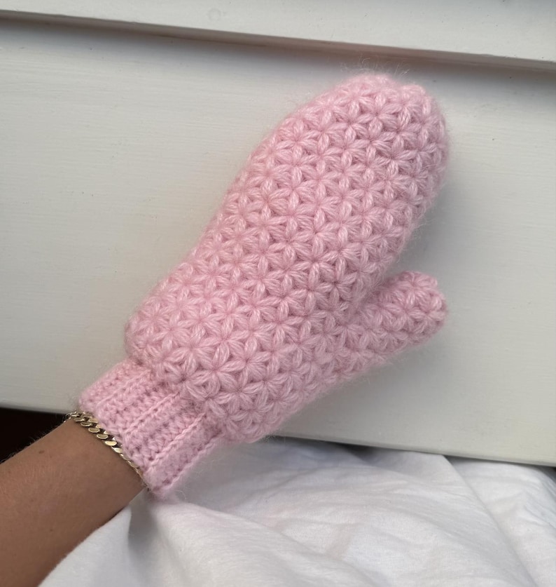 Peut inclure: Une moufle rose clair tricot&eacute;e avec un motif en &eacute;toile. Le poignet est c&ocirc;tel&eacute; et le pouce est s&eacute;par&eacute;. La moufle est faite de fil doux et semble chaude et confortable.