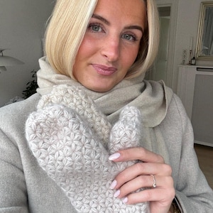 Peut inclure: Mitaines en tricot beige clair avec un motif en &eacute;toile. Les mitaines sont tenues devant une personne portant un manteau et une &eacute;charpe beiges clairs. Les mitaines sont faites d'un fil doux et textur&eacute;.