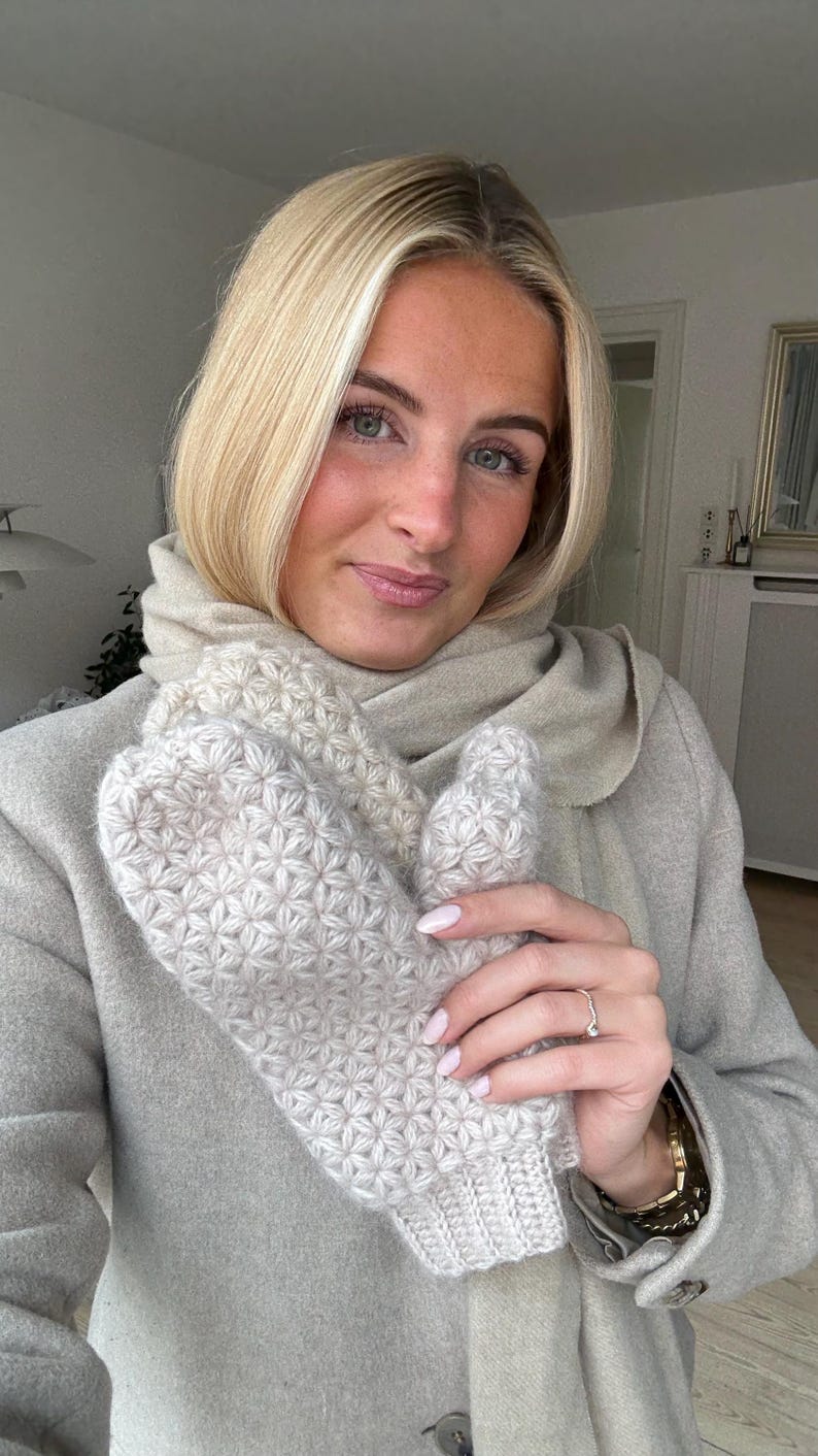 Peut inclure: Mitaines en tricot beige clair avec un motif en &eacute;toile. Les mitaines sont tenues devant une personne portant un manteau et une &eacute;charpe beiges clairs. Les mitaines sont faites d'un fil doux et textur&eacute;.