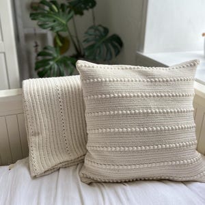 Könnte beinhalten: Eine weiße Häkeldecke und ein Kissen mit einem strukturierten Noppenmuster.
