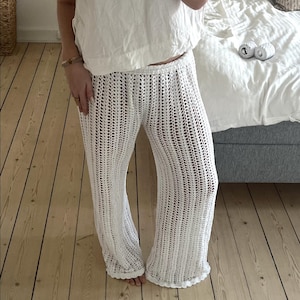 May include: White crochet pants with a wide leg and a loose fit. The pants are made of a lightweight, breathable fabric and have a delicate, lacy design.