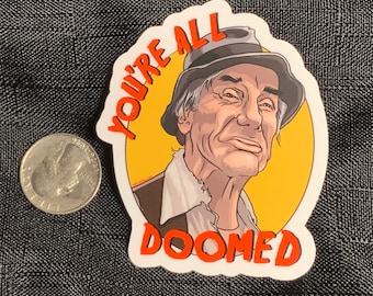 May include: A sticker with a cartoon illustration of a man wearing a hat and a yellow background. The text "YOU'RE ALL DOOMED" is written in red around the man's head.