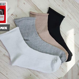 May include: Four pairs of socks in white, gray, tan, and black are arranged on a light wood surface. The socks are crew length. A red box with the text "MEDICAL EFFECT" and "011S MIX" is in the upper left corner.