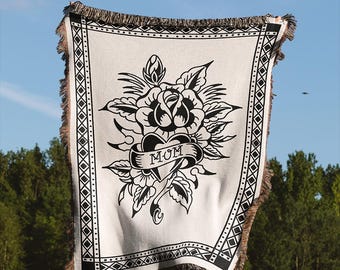 May include: A white woven throw blanket with a black and white tattoo-style design of a rose and heart with the word "MOM" on a banner. The blanket has a black and white geometric border.