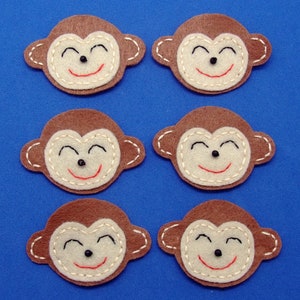 Peut inclure: Six visages de singe en feutre marron avec des yeux noirs, des bouches souriantes rouges et des yeux blancs fermés. Les visages de singe sont cousus avec du fil blanc.