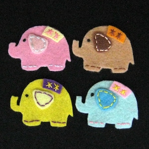 May include: Four felt elephant appliques in different colours: pink, brown, yellow, and blue. Each elephant has a different coloured patch on its back with embroidered stars.