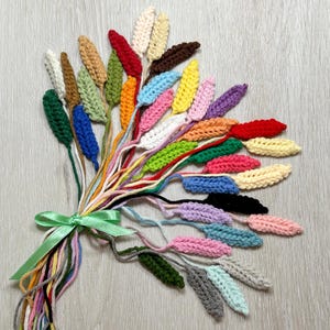 Può includere: Un bouquet colorato di fiori all'uncinetto fatti a mano in varie tonalità, tra cui rosso, giallo, blu e verde. I fiori sono legati con un nastro verde e gli steli sono fatti di filato colorato.