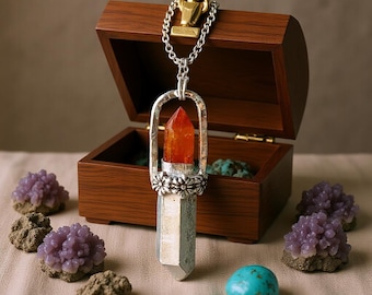 May include: A silver pendant necklace with an orange crystal encased in a decorative setting. The necklace hangs in front of a wooden treasure chest. Purple and turquoise stones are scattered around the chest.