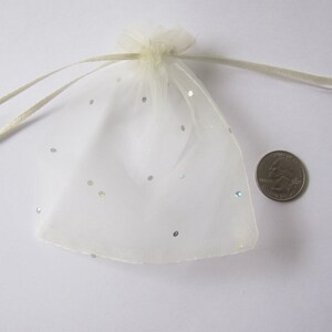 May include: A white organza gift bag with silver glitter dots. The bag is tied with a white ribbon and is approximately the size of a US quarter.