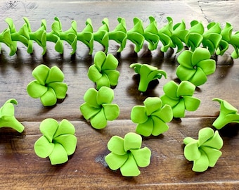 May include: Bright green floral decorations, including individual flowers and a garland, are arranged on a wooden surface. The flowers have multiple petals, and the garland is made of connected flower-like shapes.