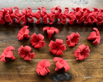 May include: A collection of vibrant red, handcrafted floral decorations. The image showcases individual flower shapes and a garland of connected flowers, all in a uniform, eye-catching red hue. These decorative elements are ideal for crafting or event decor.