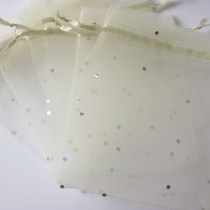 May include: A set of five ivory organza gift bags with silver glitter scattered throughout. The bags have a drawstring closure and are perfect for small gifts or favors.