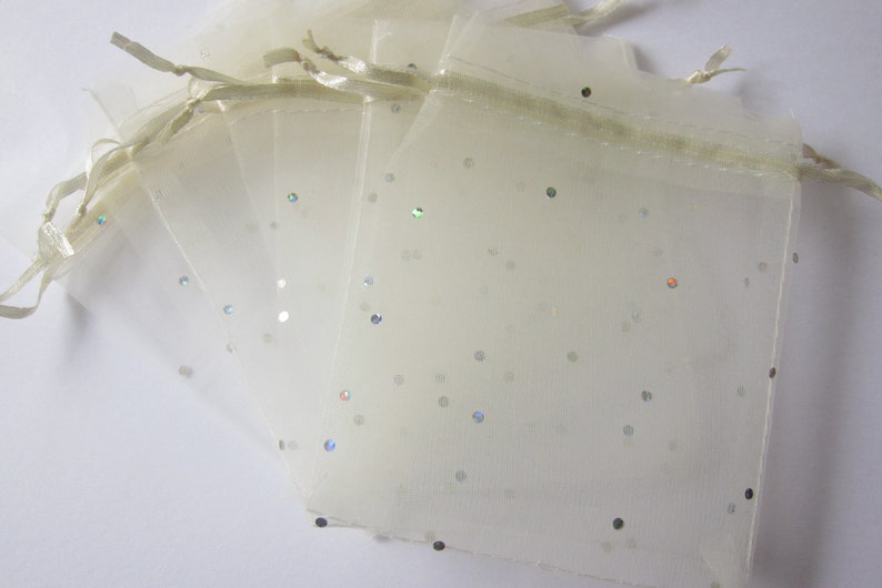May include: A set of five ivory organza gift bags with silver glitter scattered throughout. The bags have a drawstring closure and are perfect for small gifts or favors.