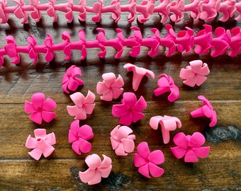 Pode incluir: Enfeites florais rosa e correntes decorativas em tons variados de rosa são dispostos sobre uma superfície de madeira. As flores estão em diferentes estágios de floração e as correntes têm um design repetitivo.