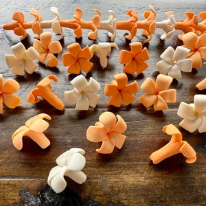 May include: An assortment of orange and white floral decorations, possibly for cake decorating or crafts, are arranged on a wooden surface. The flowers vary in size and style, with some resembling blossoms and others more abstract shapes.
