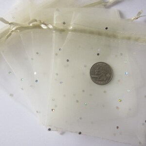 May include: A stack of ivory organza gift bags with silver glitter. The bags have a drawstring closure and are perfect for small gifts or favors.
