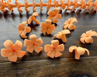 May include: Orange flower-shaped craft supplies with red centers are scattered on a wooden surface. Several flowers are in full bloom, while others are in various stages of development. A long, segmented orange piece is at the top of the image.
